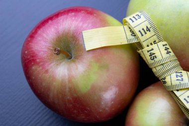 Lezzetli, Olgun elma bir ölçüm bandı sarılmış. Meyve karanlık bir tablo. Siyah arka plan.