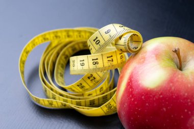 Lezzetli, Olgun elma bir ölçüm bandı sarılmış. Meyve karanlık bir tablo. Siyah arka plan.