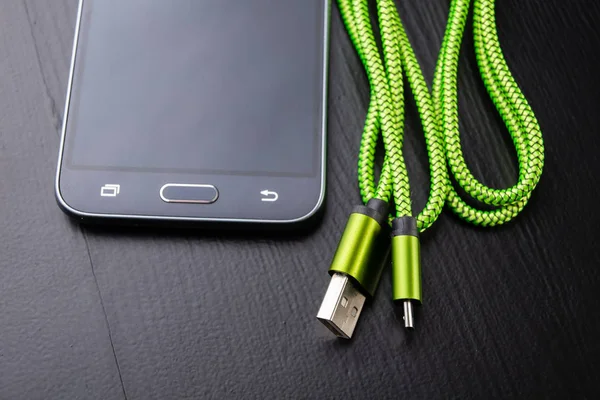 A usb cable for data transfer and phone charging. Telephone and accessories on the table. Dark background.