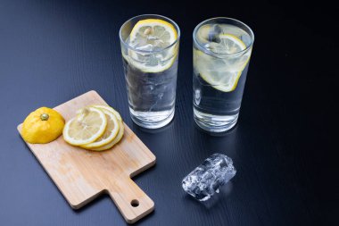 Mutfak masasının üzerine bir bardak soğuk içecek. Limon ve su bir yaz günü serinlemek için en iyi yolu ile buz. Koyu arka plan.