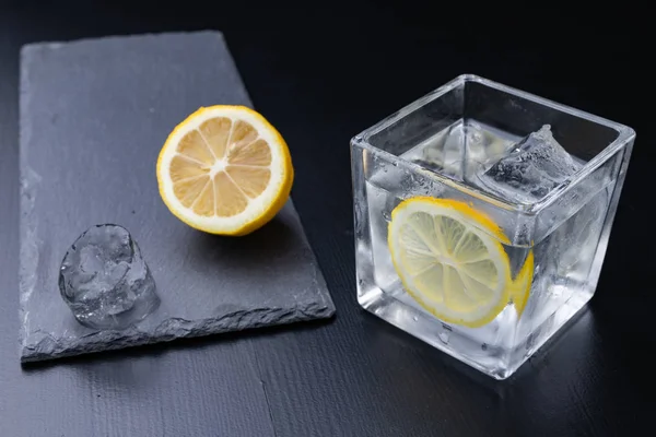 Cold drink in a glass on the kitchen table. Lemon and ice with water the best way to cool off on a summer day. Dark background.