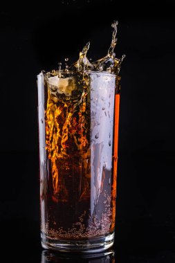 Buz ile soğuk bir içecek bir bardak içine düşüyor. Barda içki sıçrama. Koyu arka plan.