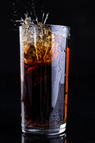 Dropping ice into a glass with a cold drink. Splash of drink in the bar. Dark background.