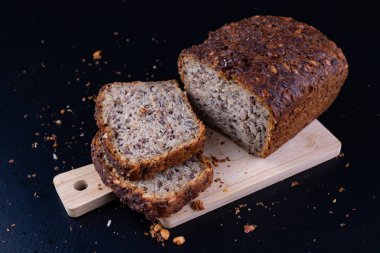 Bir ahşap tahta üzerinde tohum ekmek tatma. Mutfak masasının üzerinde taze koyu ekmek. Koyu arka plan.