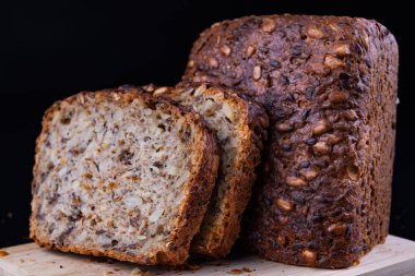 Bir ahşap tahta üzerinde tohum ekmek tatma. Mutfak masasının üzerinde taze koyu ekmek. Koyu arka plan.