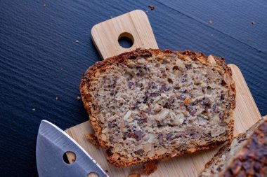 Bir ahşap tahta üzerinde tohum ekmek tatma. Mutfak masasının üzerinde taze koyu ekmek. Koyu arka plan.