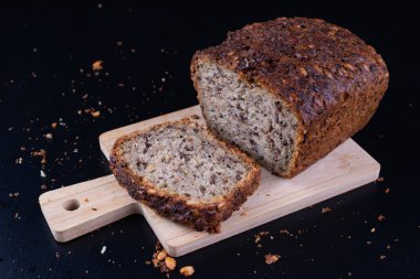 Bir ahşap tahta üzerinde tohum ekmek tatma. Mutfak masasının üzerinde taze koyu ekmek. Koyu arka plan.