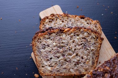 Bir ahşap tahta üzerinde tohum ekmek tatma. Mutfak masasının üzerinde taze koyu ekmek. Koyu arka plan.