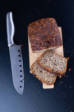 Bir ahşap tahta üzerinde tohum ekmek tatma. Mutfak masasının üzerinde taze koyu ekmek. Koyu arka plan.