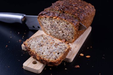 Bir ahşap tahta üzerinde tohum ekmek tatma. Mutfak masasının üzerinde taze koyu ekmek. Koyu arka plan.