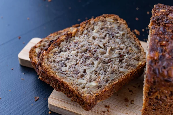 Bir ahşap tahta üzerinde tohum ekmek tatma. Mutfak masasının üzerinde taze koyu ekmek. Koyu arka plan.