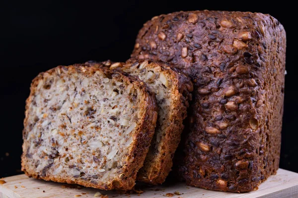 Bir ahşap tahta üzerinde tohum ekmek tatma. Mutfak masasının üzerinde taze koyu ekmek. Koyu arka plan.