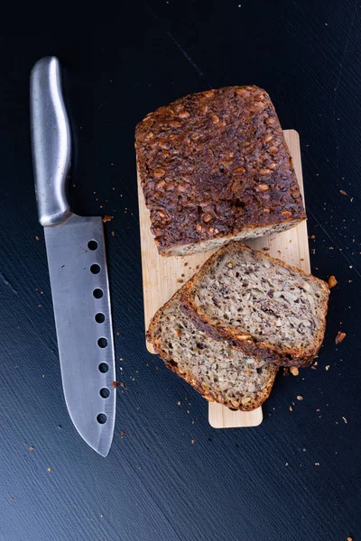 Bir ahşap tahta üzerinde tohum ekmek tatma. Mutfak masasının üzerinde taze koyu ekmek. Koyu arka plan.