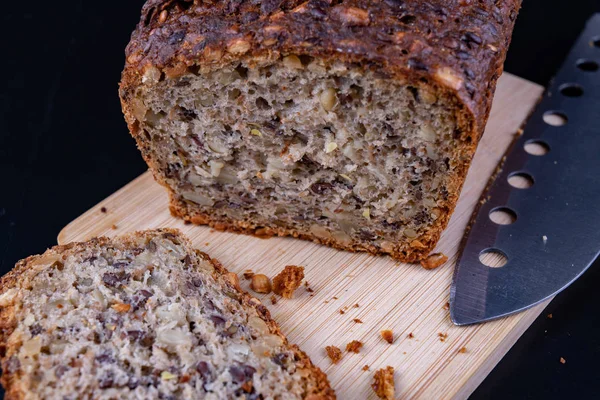 Bir ahşap tahta üzerinde tohum ekmek tatma. Mutfak masasının üzerinde taze koyu ekmek. Koyu arka plan.