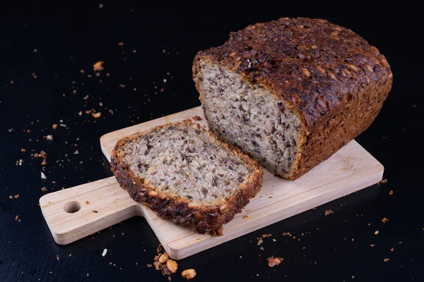 Bir ahşap tahta üzerinde tohum ekmek tatma. Mutfak masasının üzerinde taze koyu ekmek. Koyu arka plan.