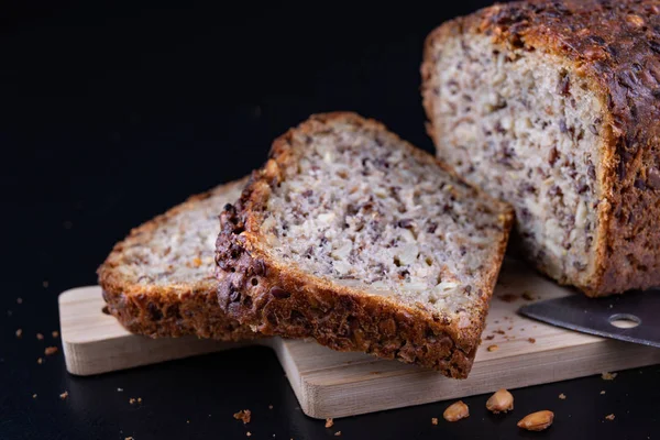 Bir ahşap tahta üzerinde tohum ekmek tatma. Mutfak masasının üzerinde taze koyu ekmek. Koyu arka plan.