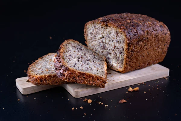 Bir ahşap tahta üzerinde tohum ekmek tatma. Mutfak masasının üzerinde taze koyu ekmek. Koyu arka plan.