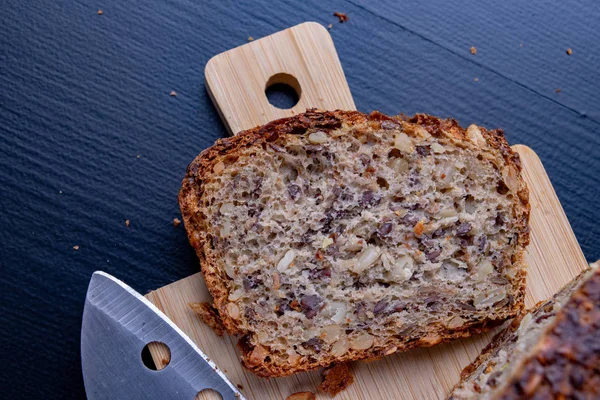 Bir ahşap tahta üzerinde tohum ekmek tatma. Mutfak masasının üzerinde taze koyu ekmek. Koyu arka plan.