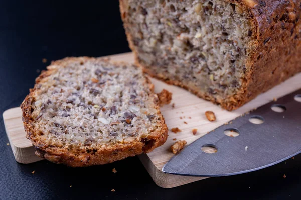 Bir ahşap tahta üzerinde tohum ekmek tatma. Mutfak masasının üzerinde taze koyu ekmek. Koyu arka plan.