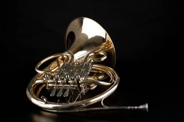 French horn on a wooden table. Beautiful polished musical instrument. Dark background. clipart