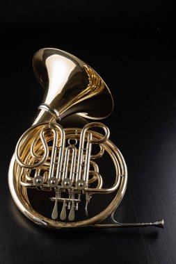 French horn on a wooden table. Beautiful polished musical instrument. Dark background. clipart