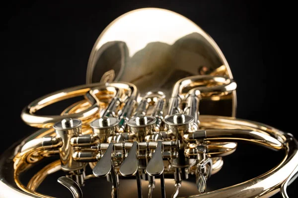 French horn on a wooden table. Beautiful polished musical instrument. Dark background.