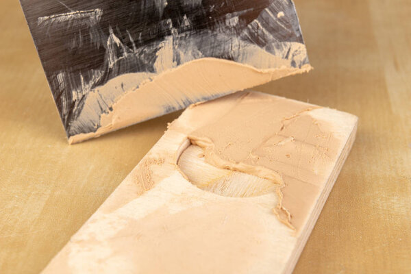 Filling compound for patching wood. Patching boards with a leveling compound. Light background.