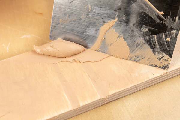Filling compound for patching wood. Patching boards with a leveling compound. Light background.