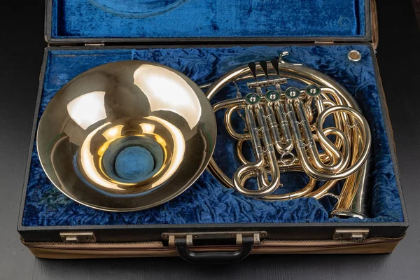 Fransız kornosu ahşap bir masa üzerinde eski bir durumda. Güzel cilalı müzik aleti. Koyu arka plan.