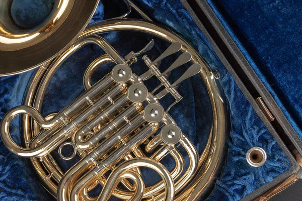 French horn in an old case on a wooden table. Beautiful polished musical instrument. Dark background.