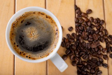 Tahta bir masanın üzerinde sade kahve olan beyaz bir kupa. Bir kahve tanesi.