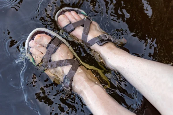 Women\'s legs in sandals soaked in the lake. Feet immersed in the