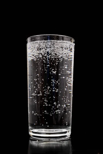 A glass of sparkling water. Refreshing mineral water in a glass dish. Dark background.