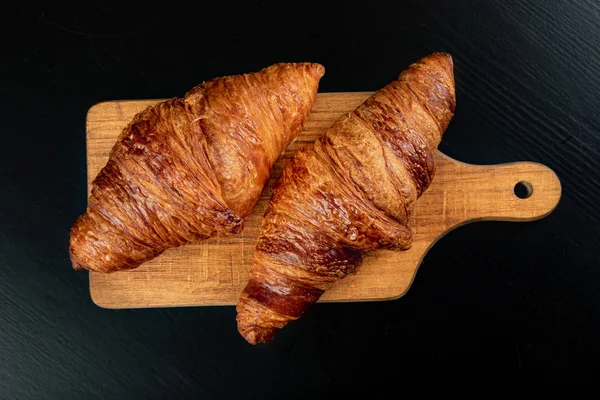 Croissant fresco saboroso em um quadro de pão escuro . — Fotografia de Stock