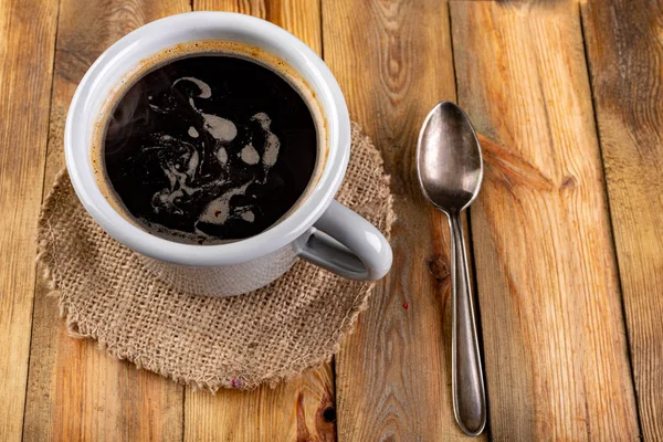 Café negro en una taza gris y una cucharadita sobre una mesa de madera. Tas. —  Fotos de Stock