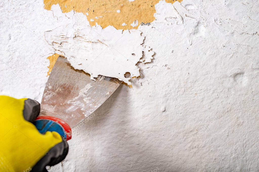 Removing old paint from the wall with a metal spatula. Small pai