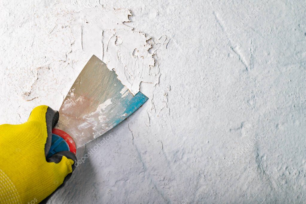 Removing old paint from the wall with a metal spatula. 