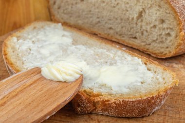 Tereyağı taze ekmekle yayılıyor. Ekmek ev mutfağında. Koyu arkaplan.