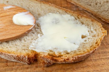 Tereyağı taze ekmekle yayılıyor. Ekmek ev mutfağında. Koyu arkaplan.