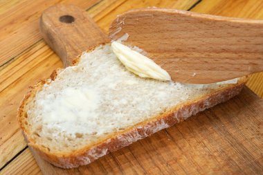 Tereyağı taze ekmekle yayılıyor. Ekmek ev mutfağında. Koyu arkaplan.