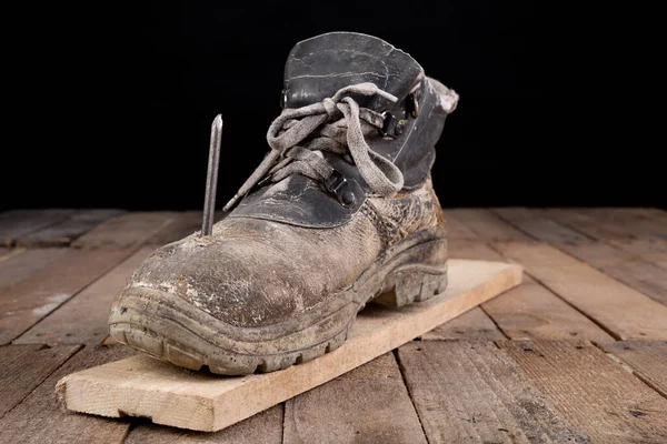 Old work shoe pierced with a nail. An accident at work when renovating a house. Dark background.