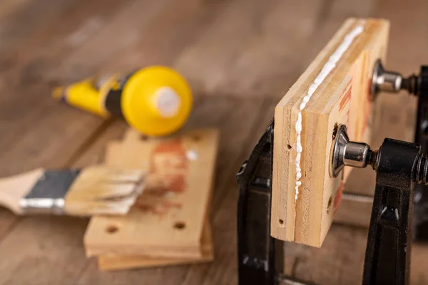 Glued wood in a carpentry clamp. Minor carpentry work in a home workshop. Light background.