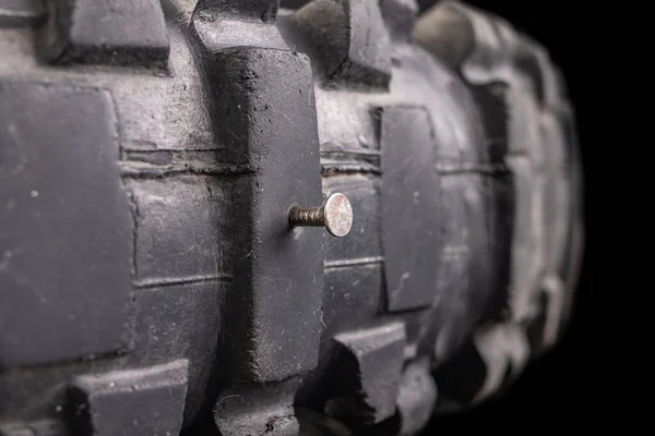 A nail in a motorcycle tire. Damaged tire with high tread. Dark background.