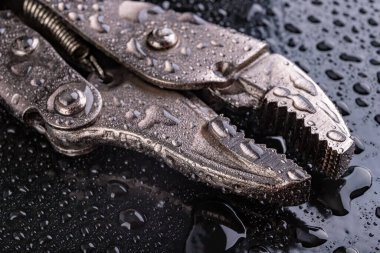 Ayarlanabilir hidrolik boru anahtarı suyla kaplı. Hidrolik teknisyenler için aksesuarlar. Koyu arkaplan.