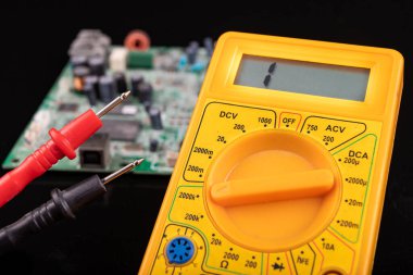 Voltmetre ve devre kartı. Bir elektronik atölyesinde ölçüm ve onarım. Koyu arkaplan.