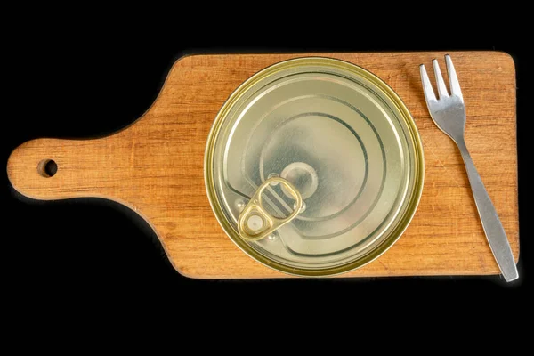 Metal can with food on a wooden board. Canned food to be eaten on the kitchen table. Dark background.