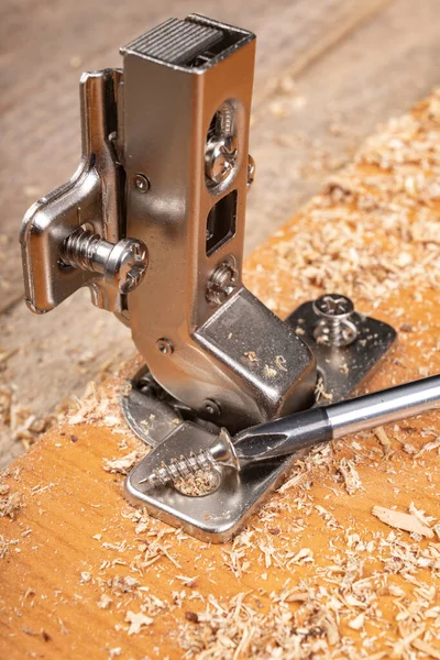 Mobilya menteşelerinin bir yonga tahtasına yerleştirilmesi. Mobilya montajında küçük marangozluk işleri. Yer - atölye.