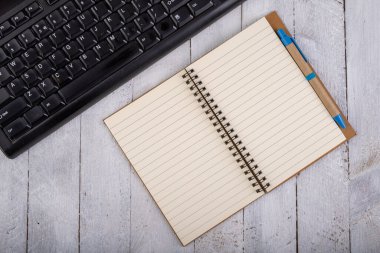 Not defteri ve bilgisayar klavyesi beyaz masada. İş için ofis aksesuarları. Hafif arkaplan.