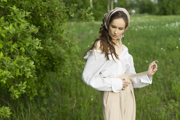 Trendy bir beyaz gömlek, bej pantolon ve bir pareo saçlarını üzerinde giyen güzel şık genç kız açık havada bir çayır ve ağaçlar karşı teşkil etmektedir. Ticari ve reklam tasarımı. Kopya alanı