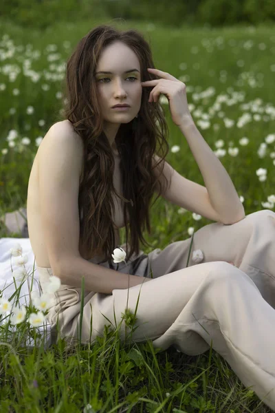 Bej jimnastik pantolonu giymiş güzel şık seksi üstsüz model kız çıplak onun meme saçları ile kapsar ve düşünceli çiçekler arasında yeşil çimenlerin üzerinde oturur. Kavramsal tasarım. Kopya alanı.